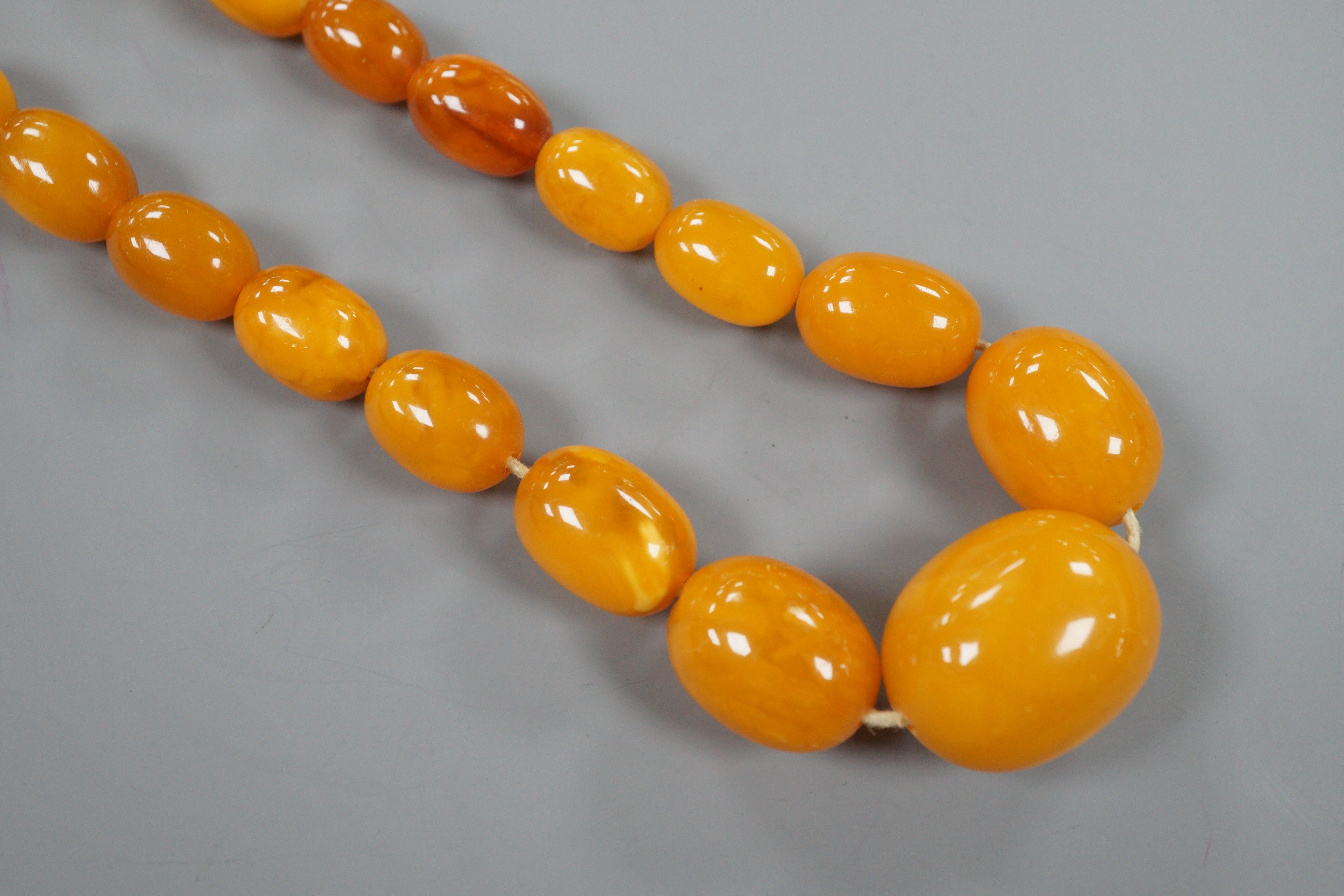 A single strand graduated oval amber bead necklace, 42cm, gross 49 grams and assorted loose amber beads, 15 grams.